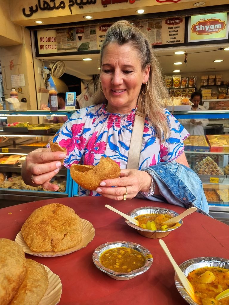 A foreigner tourist lady eating and sampling food at Shyam Sweets in Chawri Bazaar, Delhi, India. She is on a food and photography walking tour and is enjoying the delicious and varied Indian sweets. Shyam Sweets is one of the best food places in Delhi for authentic food.